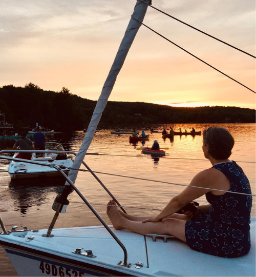 This is a photo of a woman on the hull of a sailboat at sunset