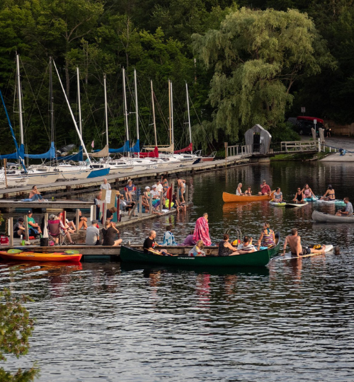 Many people gathered on a dock and in canoes listening to music